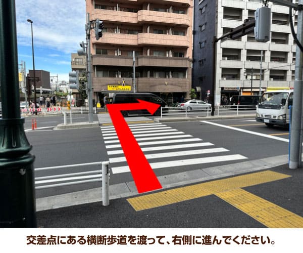 交差点にある横断歩道を渡って、右側に進んでください。